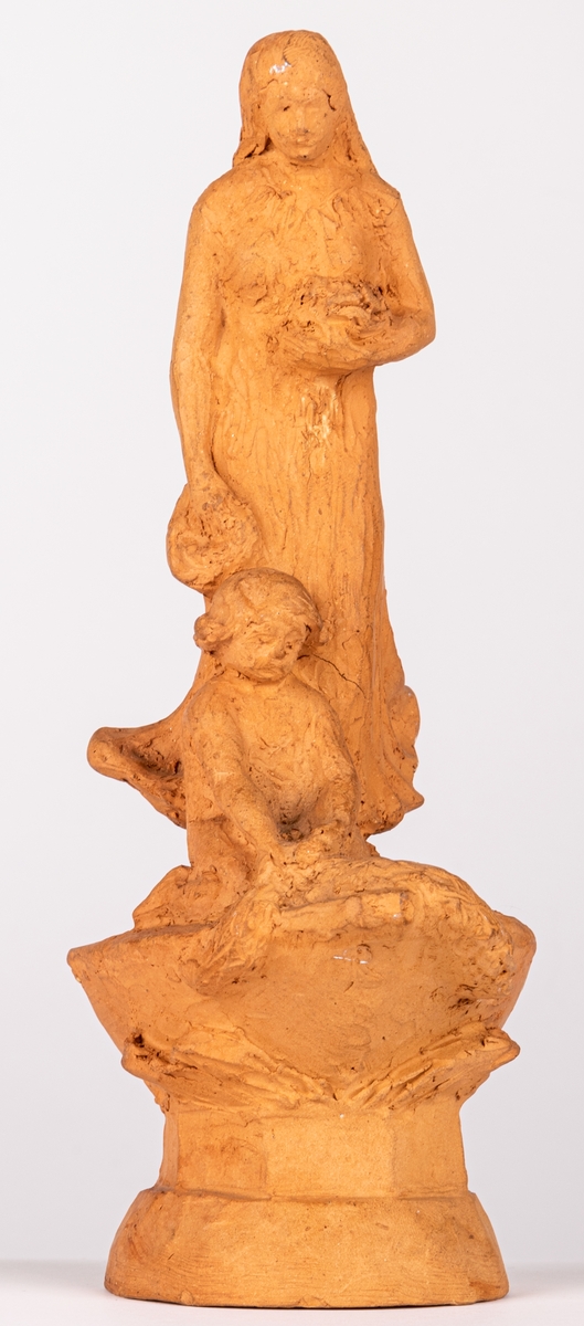 Skulpturskiss av Ida Matton till gravmonument för redarfamiljen Brodin i Gävle. Kvinna med blommor i händerna med ett barn med blomgirlang sittande framför fötterna. Båda placerade på en trekantig sockel som liknar stäven på en båt.