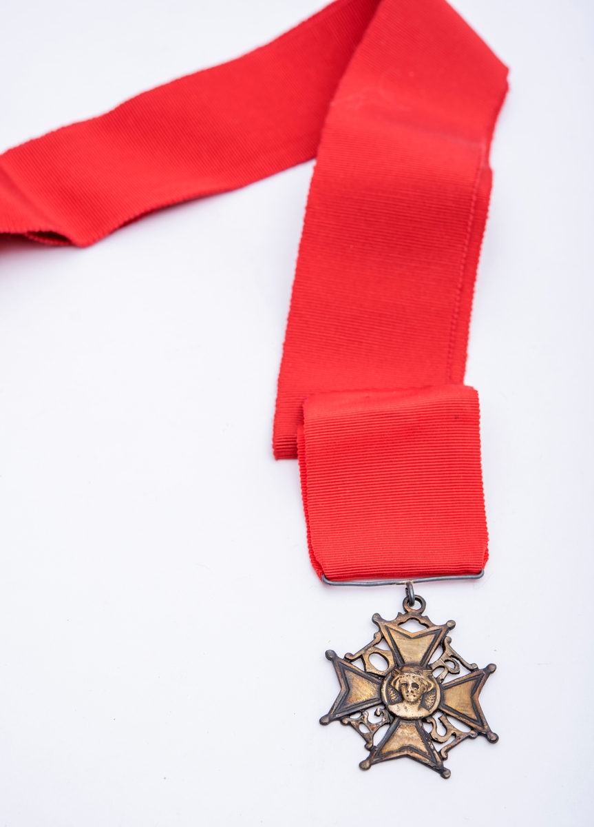 Ordensmedalje/-nål festet til rødt medaljebånd, som igjen er festet til rødt bånd til å ha rundt halsen.