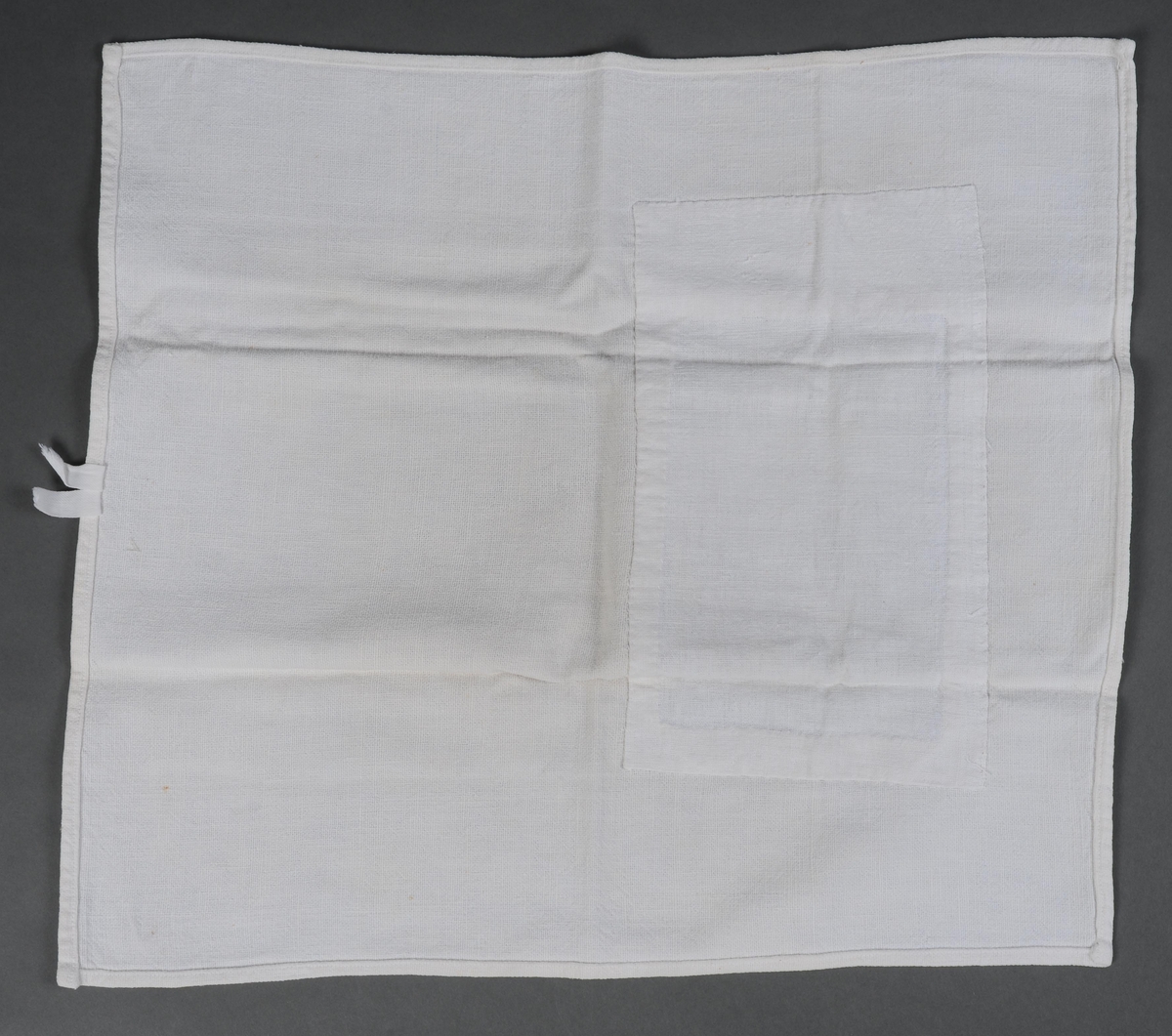 Håndduk hvor alle 4 sider er kantet inn og sydd til med maskin. Hempe av bomullsbånd er sydd på med maskin midt på den ene kortsidene. Håndduken er bødt.
