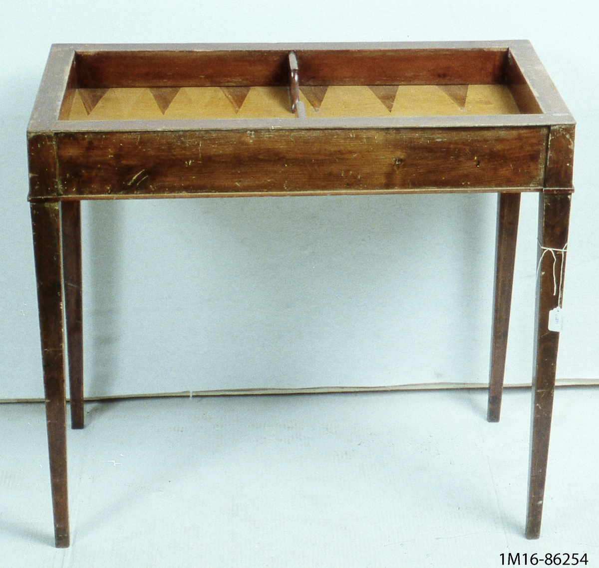 Spelbord, av mahogny, två hopfällbara skivor, raka ben. På ena skivan inlagda rutor för  schackspel och brickor.