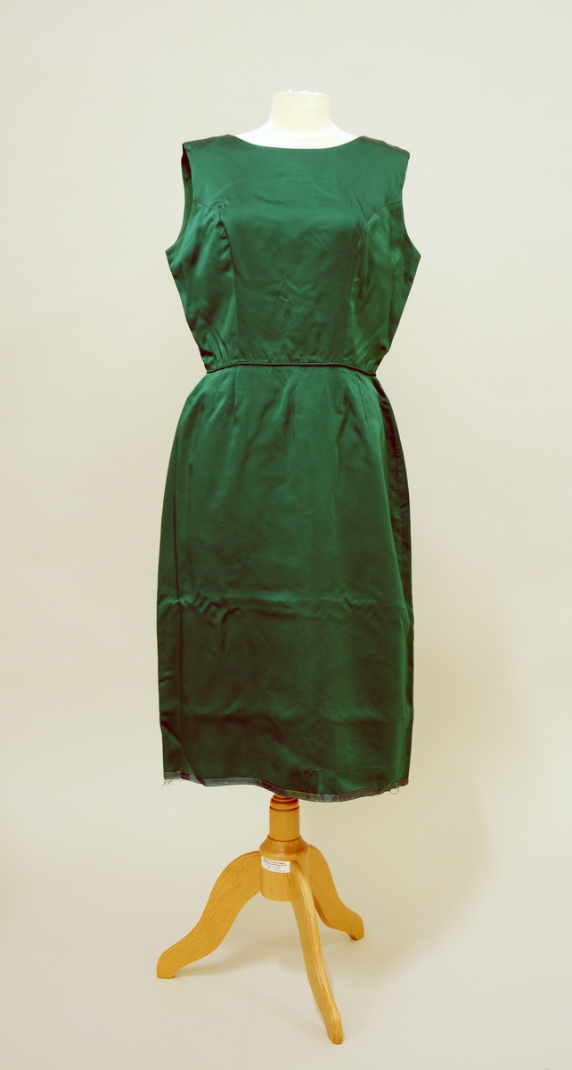 Jakke: TGM-BM.1999:0342.A
Grønn, kort jakke med 3/4- dels ermer. Åpning foran, to knapper formet som knuter i samme stoff. Innvendig fòret med gul fòrsilke.

Kjole: TGM-BM.19990342.B
Grønn, figursydd kjole uten ermer. Glidelås bak.