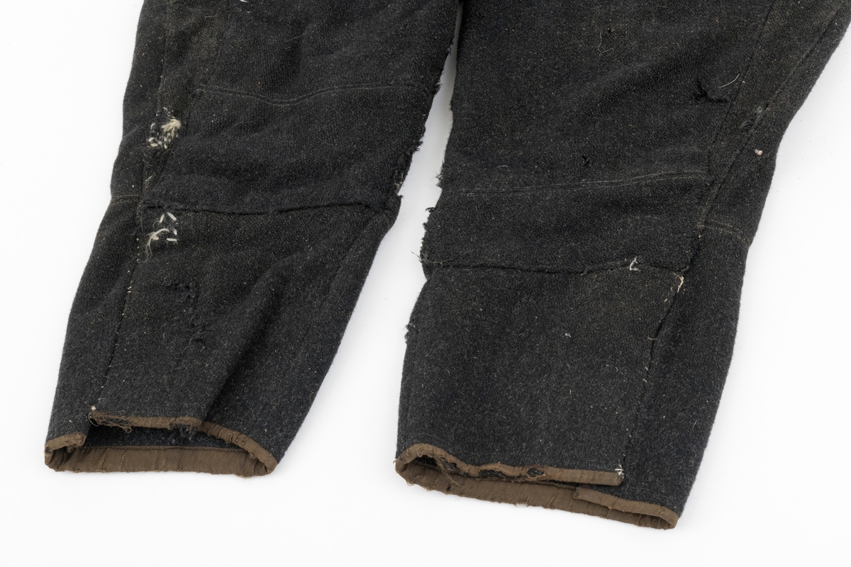 Vadmelsbukser som har vært brukt i 1920-30 åra. Innvendige lommer av bomullsstoff. Buksa er antagelig hjemmesydd. Stoffet på innsiden av linningen er i kunstsilke.