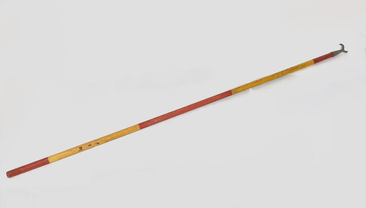 Båtshake, bestående av en stång i trä målad med gula och röda ränder. Samt med en s-formad krok av metall i ena änden. Märkt vid sidan "2 - 4" med svarta bokstäver.