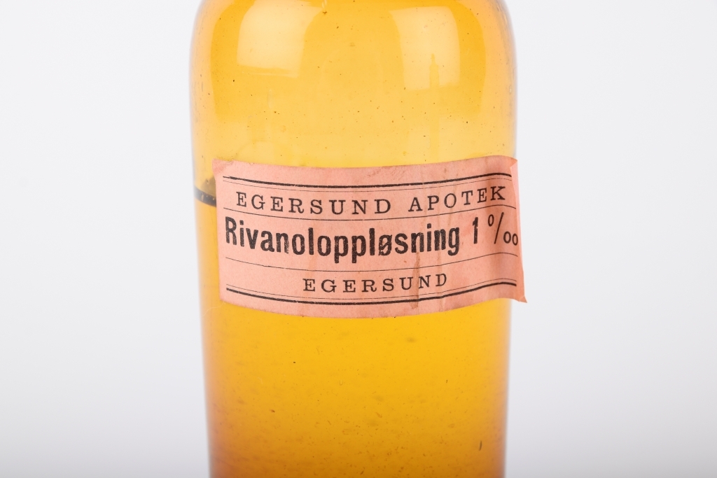 Medisinflaske med rivanoloppløsning fra Egersund Apotek. Rivanol er et desinfiserende middel.

Gulgrønn flaske med kork. Pålimt papiretikett.