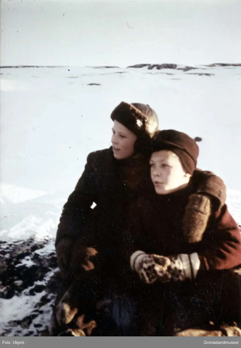 To unge gutter sitter på en knaus i et snødekt landskap.