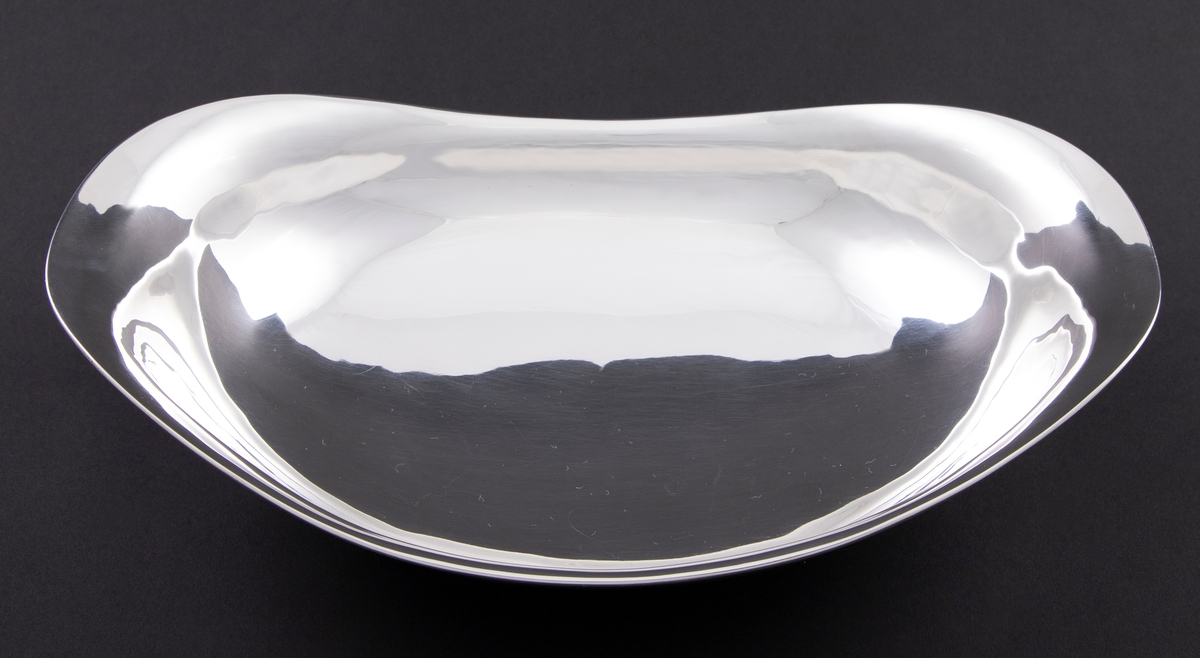 Oval skål i sølv. Langstrakt korpus med mykt buet profil og oppadsvungede sidepartier, som hviler på en lav oval fotring.