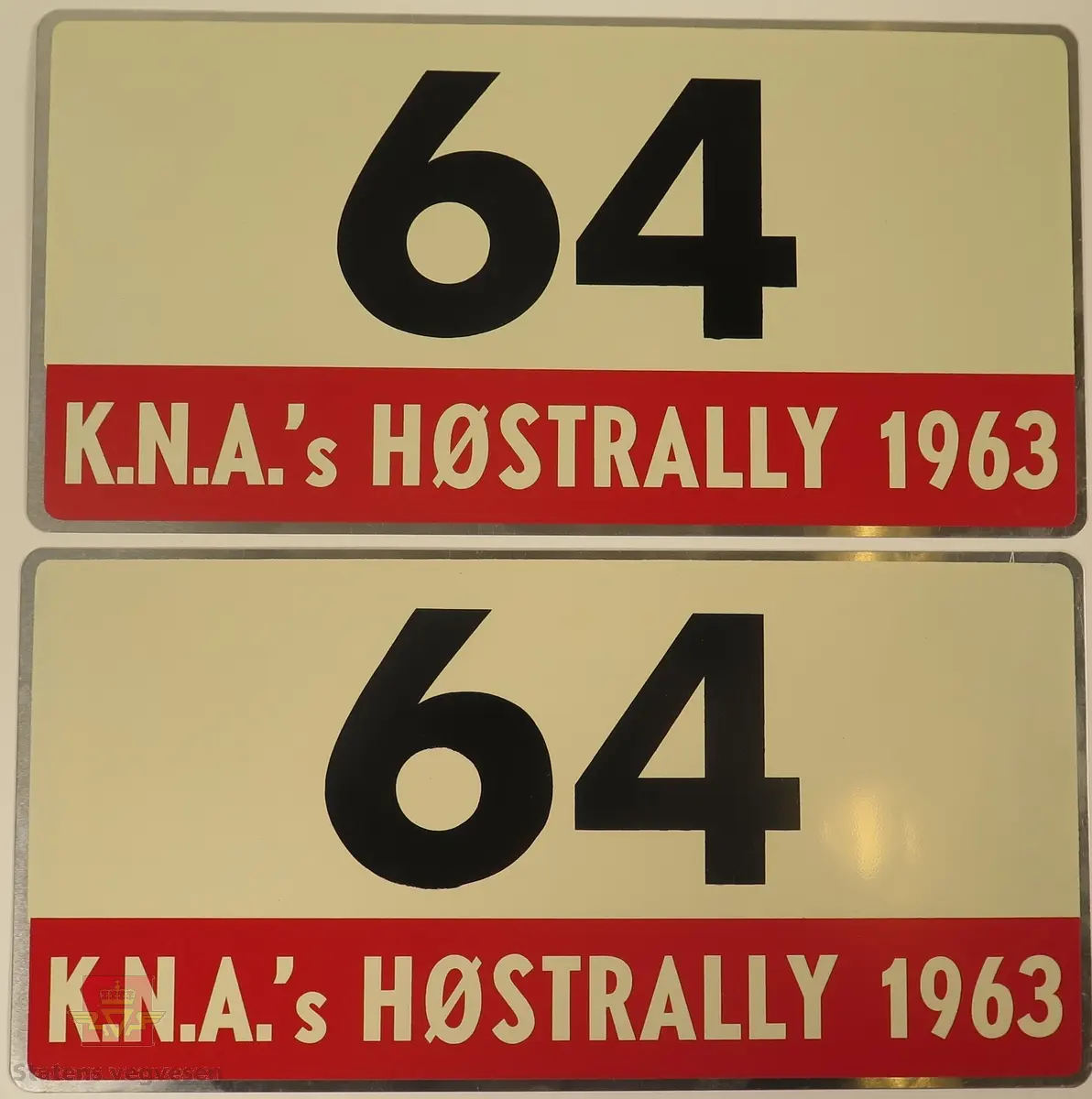 Hovedsakelig hvite metallskilt med et mindre rødt markeringsområde. Grupperingen med skilt har også nummeret "64" påført seg, dette er en indikasjon på deltakernummer.
Påskrift: K.N.A.'s HØSTRALLY 1963