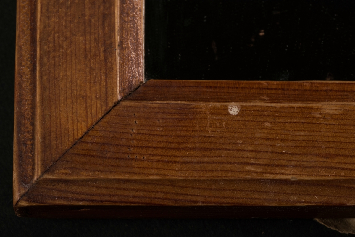 Rektangulär rakspegel med träram. Upphängningsögla med ett rött snöre.
Det finns inprickat mönster med nål i form av två hakkors på baksidan, samt troligen ett påbörjat hakkors på ramens framsida.