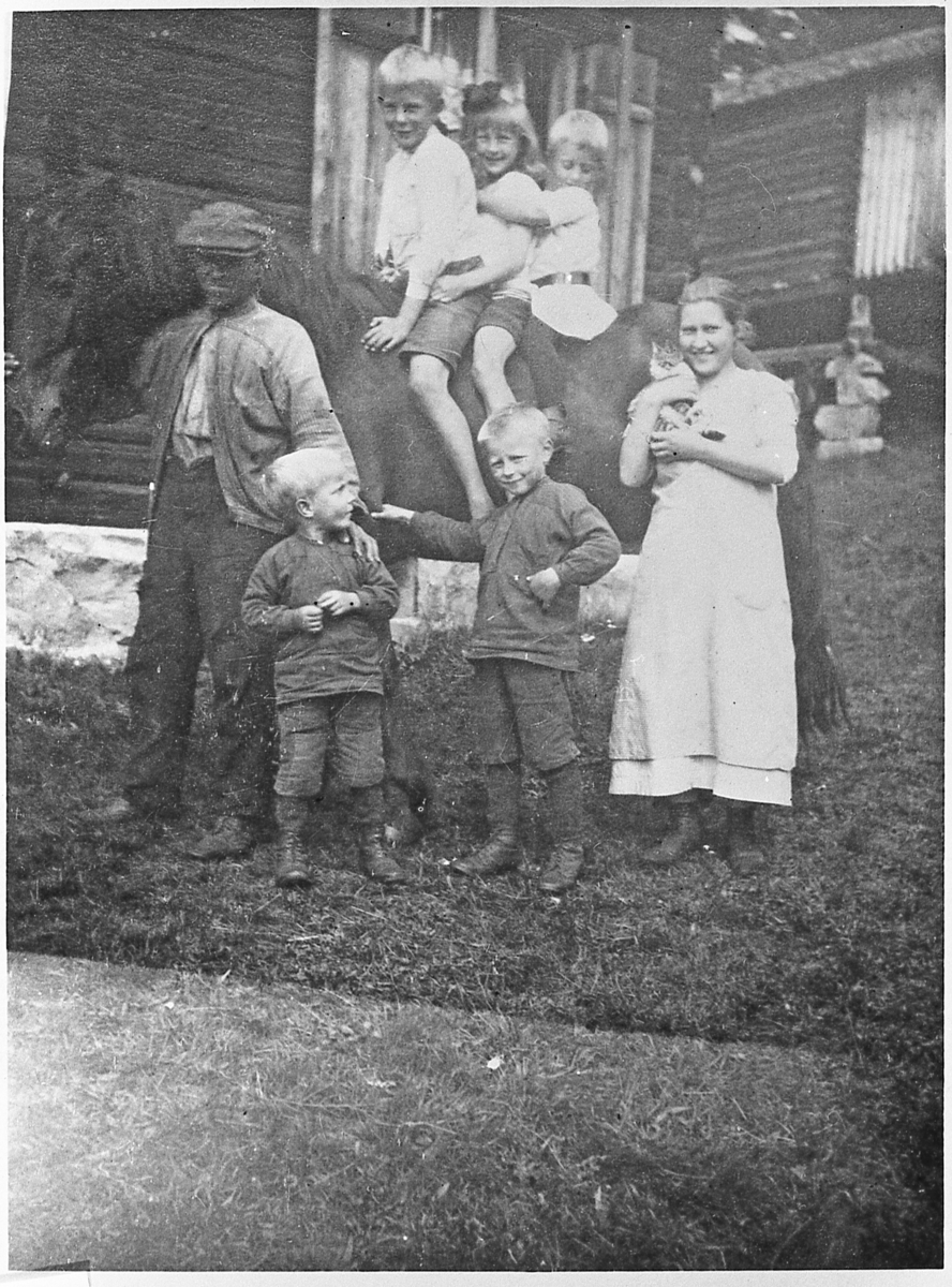 Åsen på Grenskogen, 1918. Engebret Flågan holder hesten, en ukjent kvinne med katt. Mange barn.
