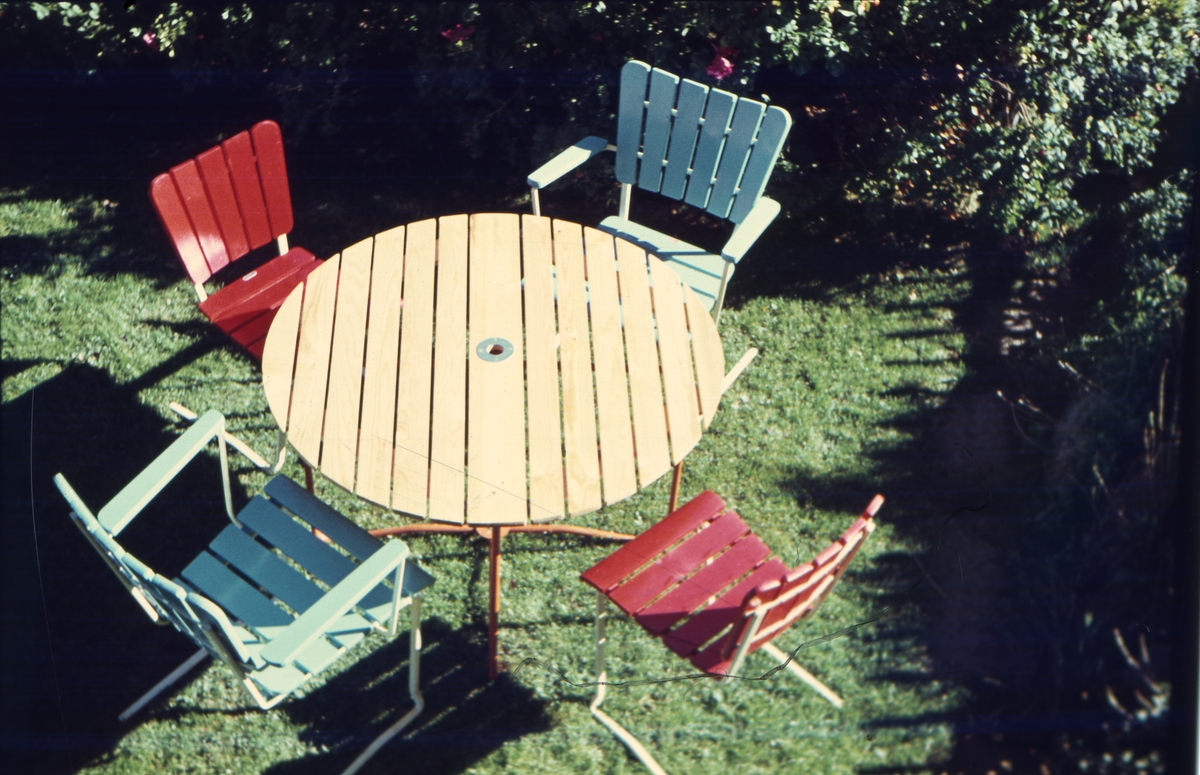 Trädgårdsbord och stolar i trä och fjäderstål. De är målade i glada färger.