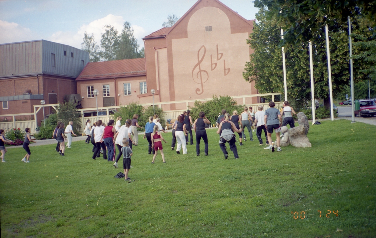 En grupp människor deltar i ett gymnastikpass på gräset utanför Bollnäs musikskola, 24 juli 2000.