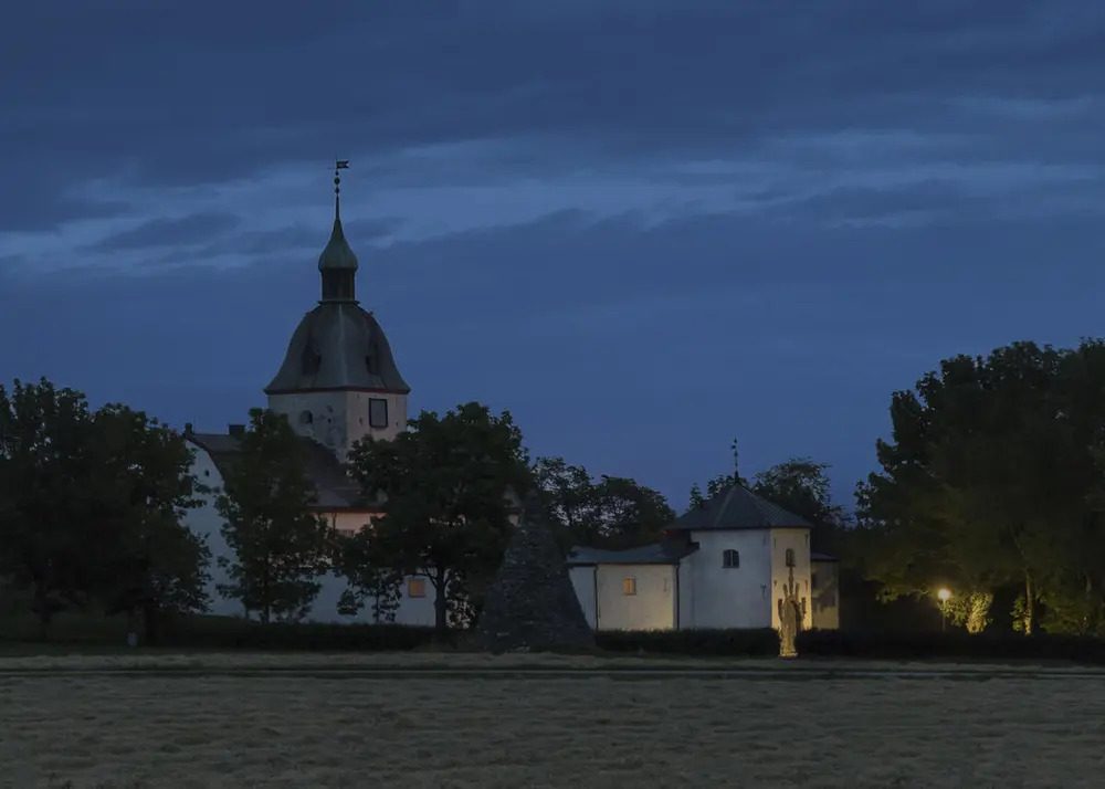 Austråttborgen i landskap. Det er mørkt og ei gatelykt lyser opp inngangsportalen. Mørke trær dekker deler av borgen.