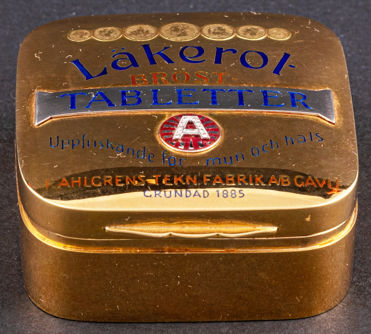 Tablettask i form av en Läkerolask, i guld med ädelstensinfattning i form av briljanter inlagda i bokstaven A på locket.