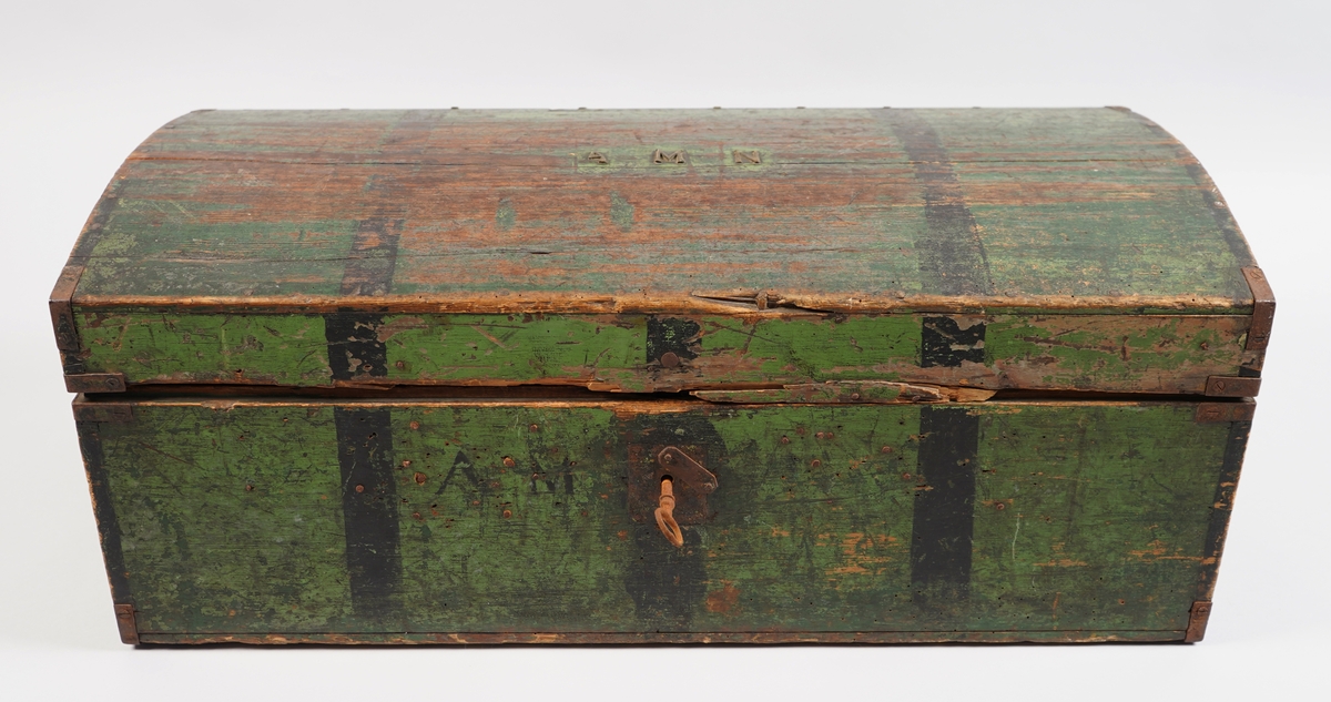 Ein grønmåla koffert i tre. Loket er forma av eit bord og er boga. Hjørna er halde saman med nokre "sinktapper" samt forsterka med metallvinkler. Kofferten har lås, og handtak i båe ender.
