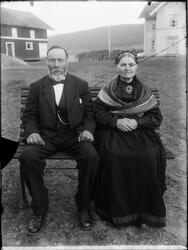 Portrett av mann og kvinne som sitter på en benk i gårdstune