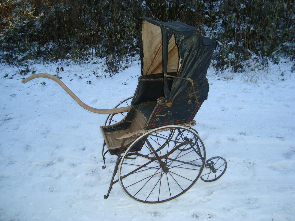 Barnvagnen är en sittbarnvagn med en fällbar sufflett. Barnvagnen har två stora framhjul och två små bak. Den har två ben för att den inte kan  tippa fram. Med det höga handtaget kan den rulla fram- eller bakåt. Barnvagnen är svart med dekoration i form av röda raka linjer.; Den kommer från Kempefamiljen som bodde på Sanna på Hemsön. 