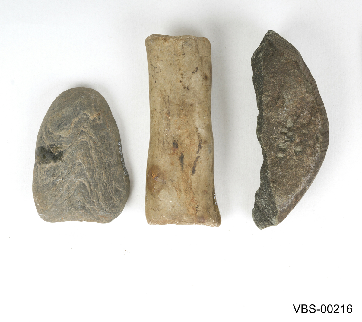 Sett med tre steinverktøy i forskjellige former og størrelser:
(a) Ett stein er langstraktog smalt.
(b) Ett annet avrundet og bearbeidet i en konkav form som redskap.
(c) Det siste ser ut som et ødelagt fragment av en større, i form av en bolle.