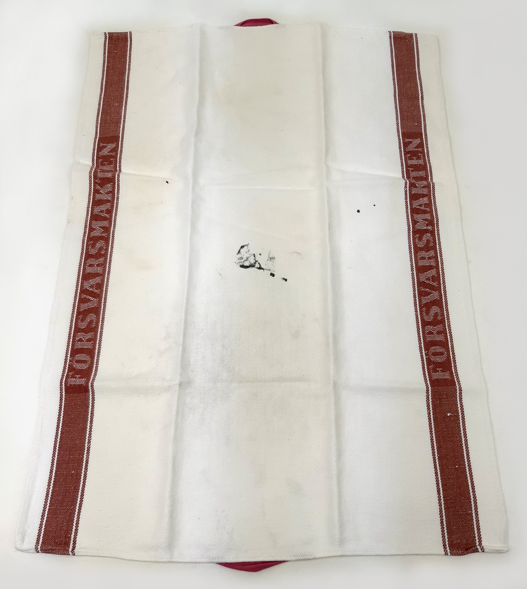 Linnehandduk i vit textil med bruna bårder, samt invävd text "FÖRSVARSMAKTEN".