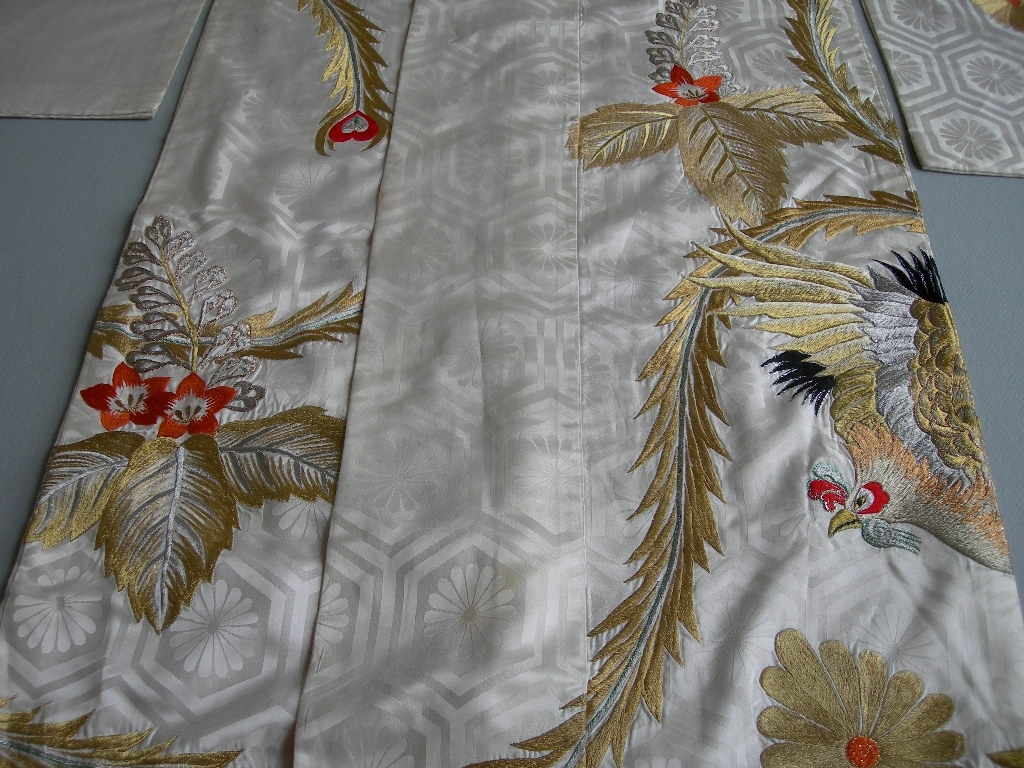 Kimono av vit viskos, mönstrad med jaquardvävd blomma i en sexkantig ram.
Bakstycket består av två våder 31 cm breda. Varje framstycke består av en 26 cm bred våd med en 15 cm bred framkant och en 12 cm bred nacklinning som går ned över bröstet. I nederkanten 6 cm bred valk av rött viskostyg (samma som fodret), fylld med bomullsvadd. Ärmar 104 cm långa och 31 cm breda.
Maskinbroderier i guld-, silver- och glitterfärgad tråd samt svart, röda och oranga detaljer. Blom- och bladmönster samt två fåglar.
Foder: rött viskostyg.