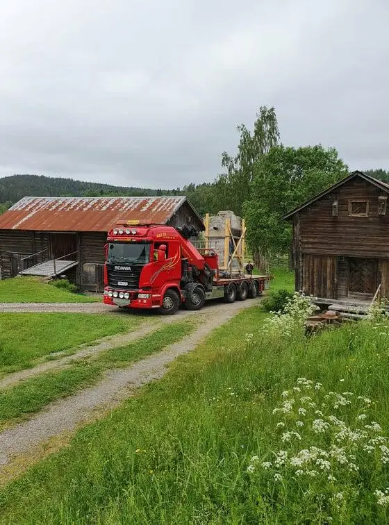 En rød lastebil på veg opp tunet. Lastebilen frakter essa.