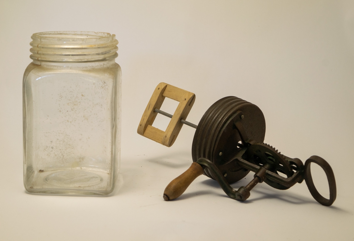 Kvadratisk glassbeholder med skrulokk som er forsynt med en håndvisp, hvor selve vispen er i tre.