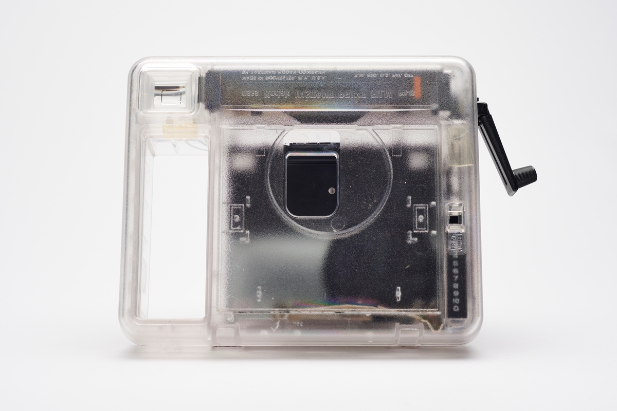 Kodak EK2 Instant Camera, også kalt The Handle, i gjennomsiktig plast. Kameraet er utstyrt med bl.a. autofokus, manuell bildeutløser, mulighet for avtagbar blits og anvendte Kodaks egen PR10 instant film. Kameraet er produsert av Kodak og er en av få som har fått beholde sitt originale navnemerke, da dette kamera mest sannsynlig aldri ble solgt, men har fungert som et visningseksemplar i butikk.  
Polaroid fikk på alvor en konkurrent på markedet da Kodak begynte å produsere instant kameraer og film i 1976. På 1960-tallet hadde Kodak produsert film for Polaroid, men nå var stemningen en annen. Dette var ikke et samarbeid og Polaroid, som hadde patent på produktet, svarte med å gå til rettssak. Det var en langvarig rettssak. Kodak ble nødt til å trekke sine instant-produkter fra markedet i 1986. I 1990 var erstatningssummen avklart og året etter måtte Kodak betale Polaroid 925 millioner amerikanske dollar (inkludert renter). Dette var den største erstatningssummen noen gang frem til 2012. I tillegg måtte Kodak kompensere sine kunder som hadde kjøpt instant kameraer av dem fra 1976 til 1986, da de nå ikke lenger fikk kjøpt film som passet. Kunden ble bedt om å ringe et gratisnummer og registrere seg for å få tilsendt en pakke i posten, som inneholdt instrukser for hvordan de kunne få kompensasjon. Ofte involverte dette at de måtte ta av kameraets navnemerke og sende tilbake som et bevis for at de eide kameraet. I dag er instant kameraer fra Kodak uten navnemerket mer vanlig enn med.