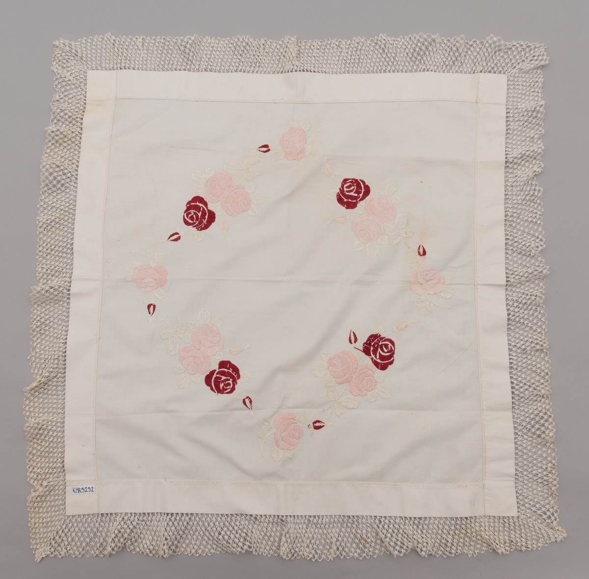 Duk, brodert kaffeduk i bomull med roser i fargene rød og rosa med blader i hvitt plattsøm, heklet blonder 5 cm brede påsydd i kantene