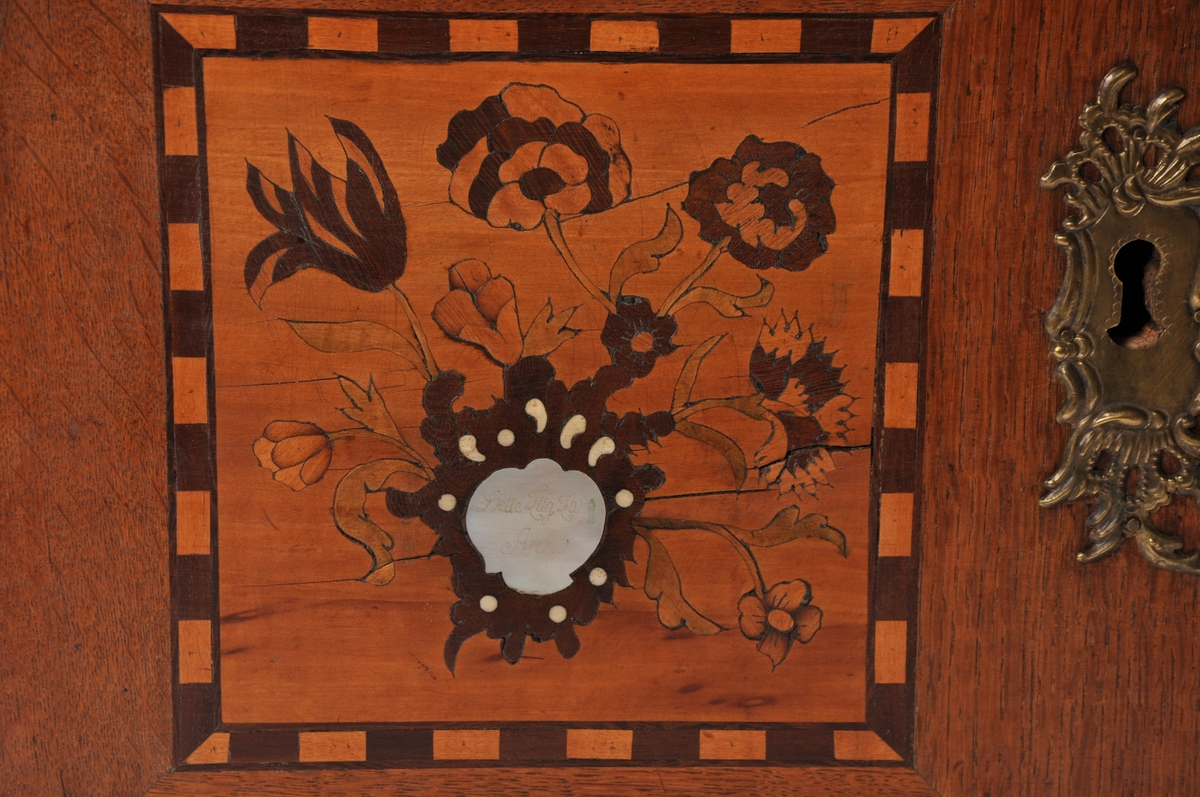 Fredrikshalds liklaugs kiste i tre, med intarsia dekorasjoner. På forsiden innsatt med perlemor med inskripsjon. På lokket en dødningsskalle i ben. Med  håndtak i messing.