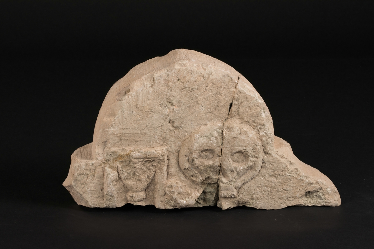 Fragment av gravsten, dekorerad på båda sidor.
Framsidan föreställer en ängel i en cirkel.
Baksidan föreställer en dödskalle och ett timglas. Endas halva timglaset är bevarat.