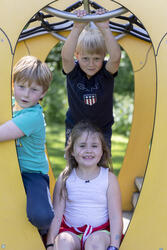 Nærbilde av tre små barn som leker i et klatrestativ i parken bak Wergelands Hus