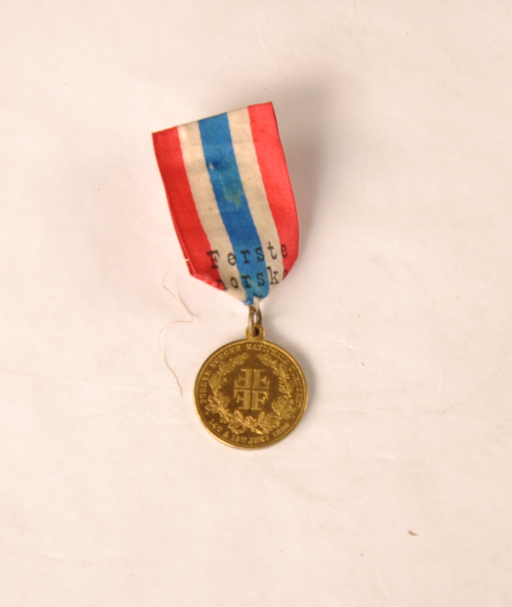 Medalje til Edv. Thoresen fra det første norske nasjonale turnstevnet 15. juni 1886. Henger i et bånd med de norske fargene og påskriften Første norske nationale turnfest.