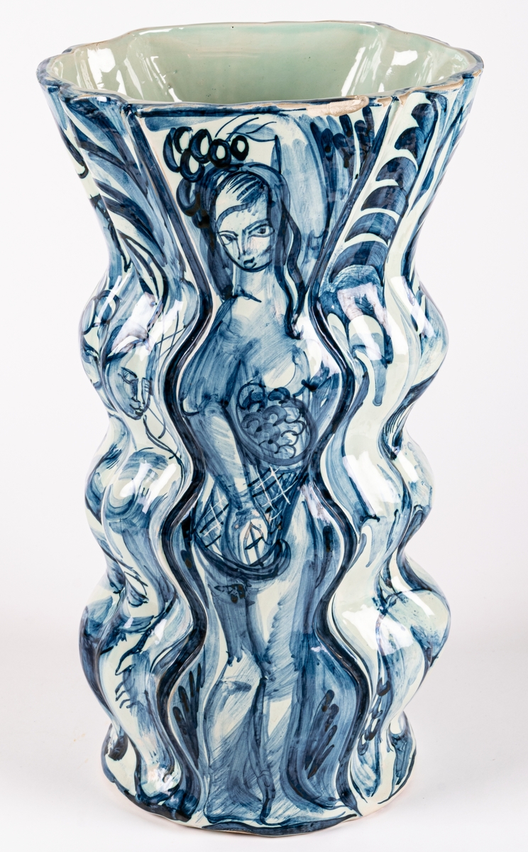Vas, Bo Fajans, design Allan Ebeling. Vasens form är vågformad med en trattliknande avslutning, blå figurdekor på grå tennglasyr, växter och kvinnofigur.