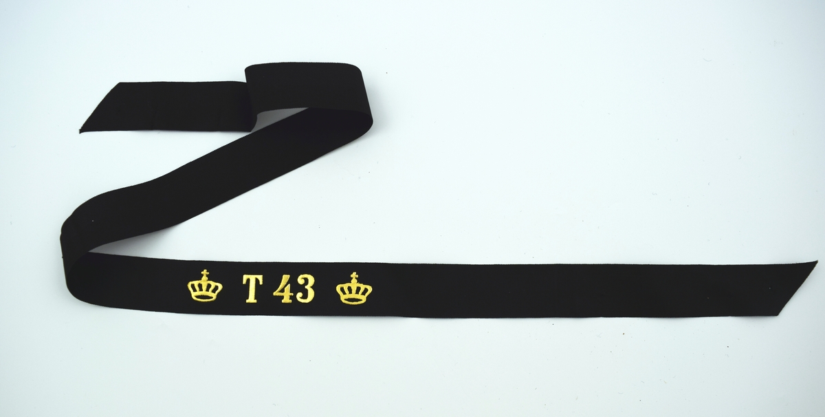 Mössband av svart sidenrips. Guldfärgad text, "T 43", med två kronor på vardera sida.