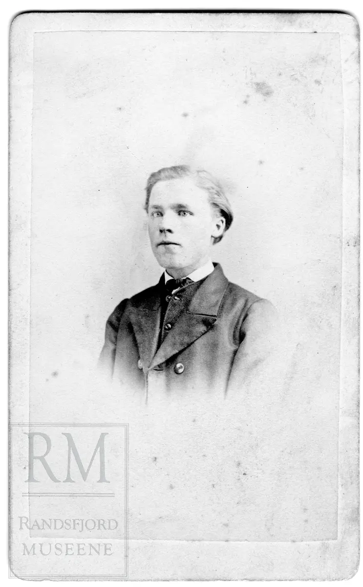 Brystbilde av ung mann i jakke med store slag og sløyfe i halsen.