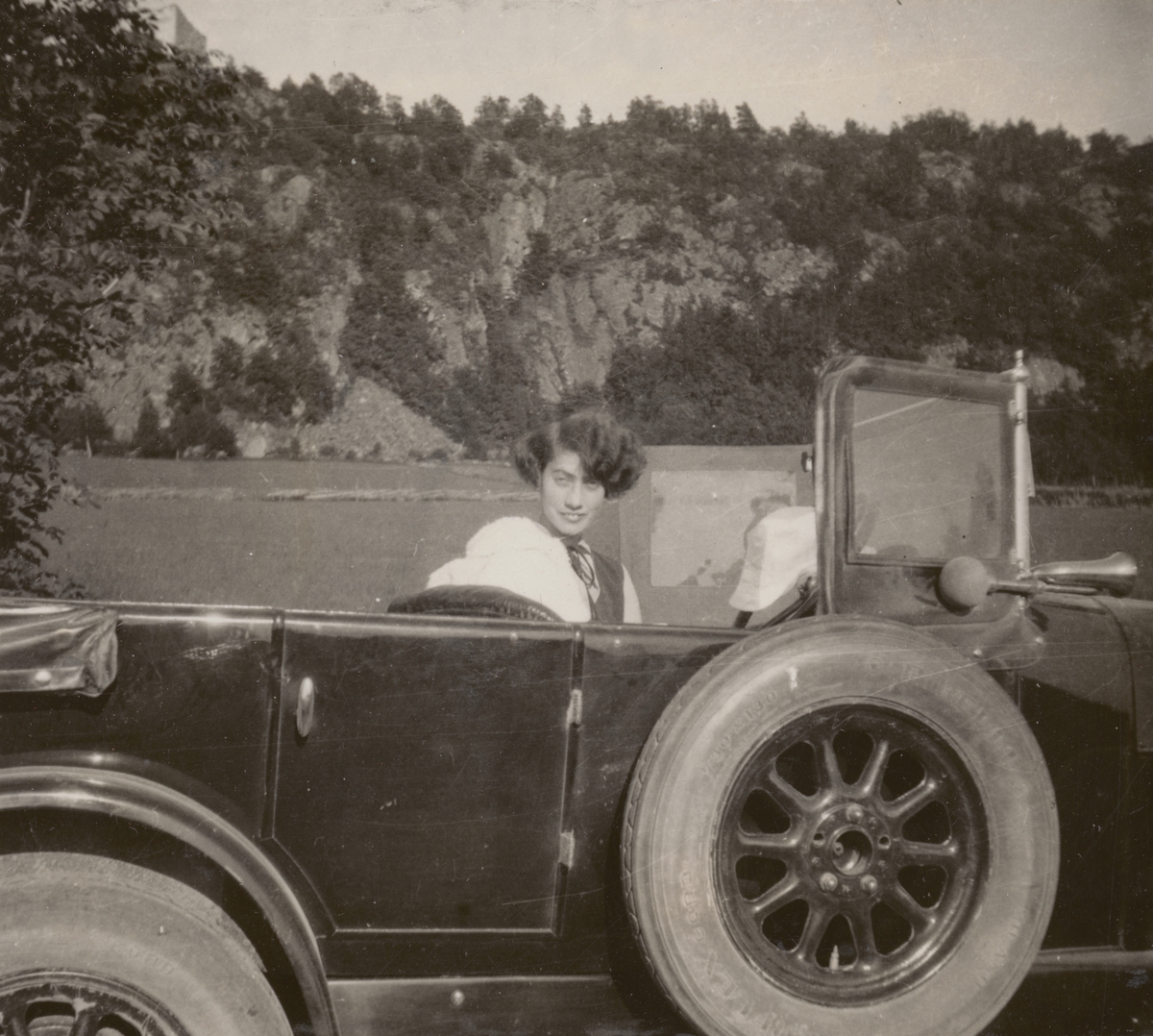 Anna Linderstam sitter i en bil på en väg nedanför Brahehus, 1925.

Text vid foto: "Med Fiat 501 på strövtåg i vida världen. 1925. X Brahehus. Flickan."
