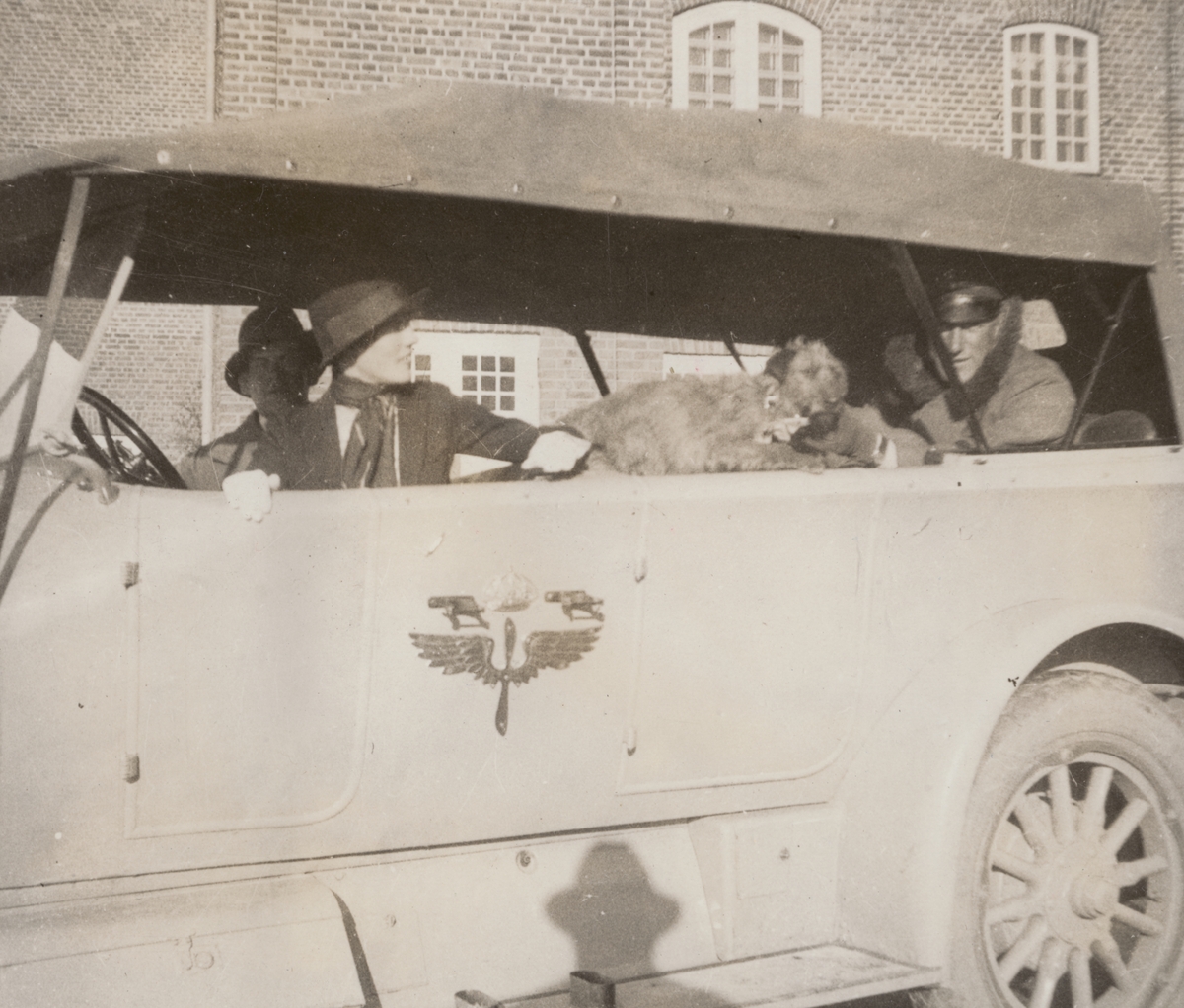 Tre personer och en hund sitter i Flygkompaniets bil, cirka 1925. Mannen till vänster är militären Birger Schyberg, mannen till höger är militären Nils Kindberg. Kvinnan heter Anna Linderstam.

Text i album: "Jan. 1925. Strängnäs. Birger. AL. NK. Muffsie."