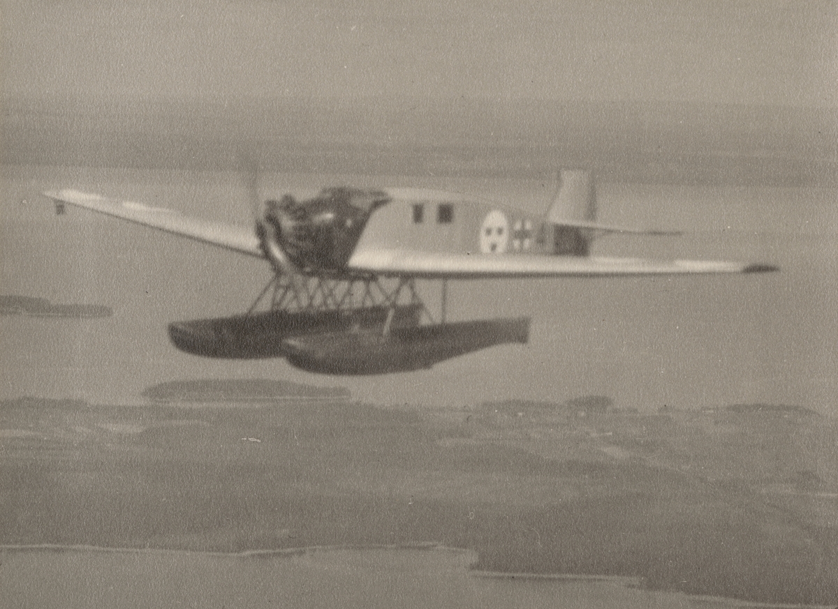 Ambulansflygplan Trp 2, Junkers W 33 märkt nummer 4 i luften över skärgård. Flygbild, vy från sidan.