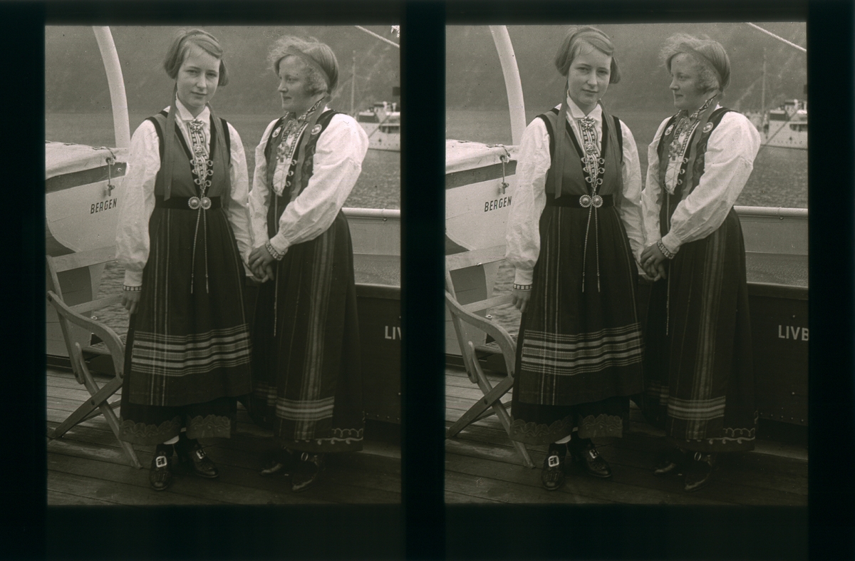 To jenter ikledd Sognebunad reiser med båt. Tilhører Arkitekt Hans Grendahls samling av stereobilder.