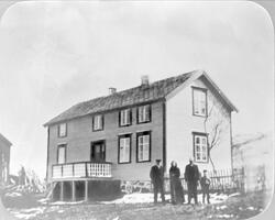 Fire personer på et gårdstun foran våningshus på Bremnes.