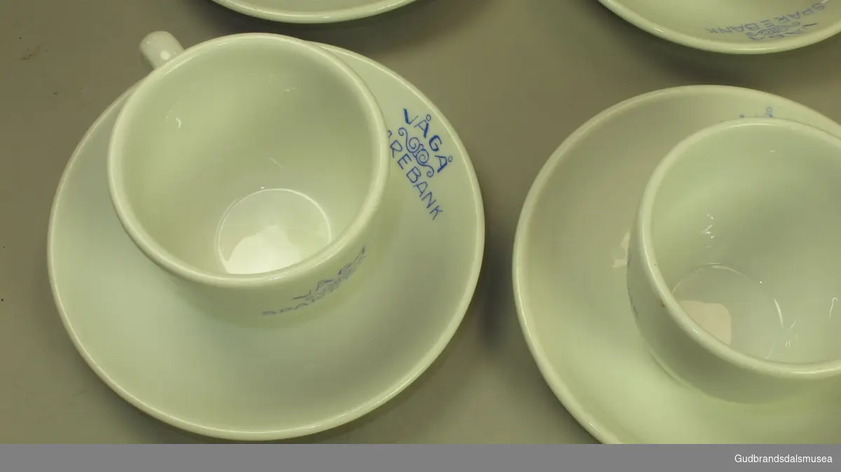 Seks kaffekopper med skål. Blå påskrift. To kopper har en sprekk.