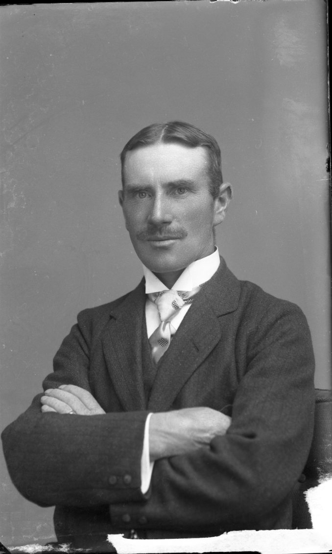 Porträtt av en man med mustasch och slips. Han håller armarna i kors.