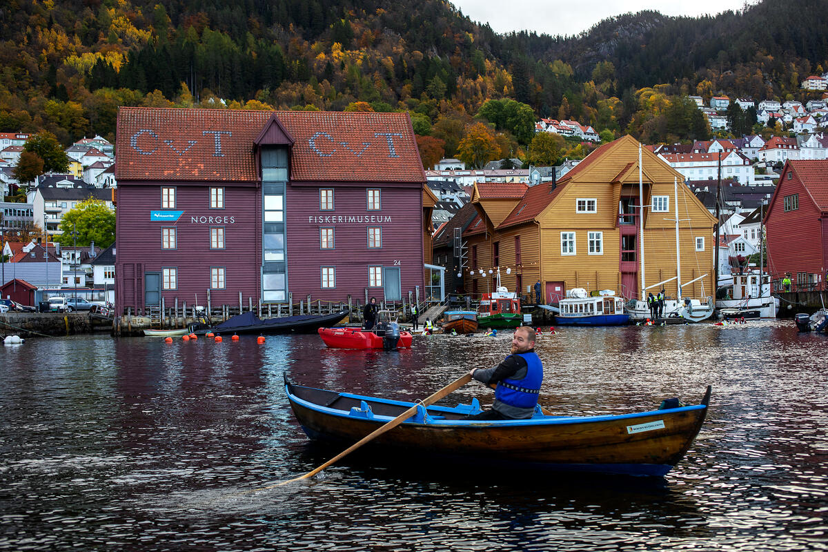 Havnen foran Norges Fiskerimuseum en fin høstdag, og en mann i robåt ror i forgrunnen