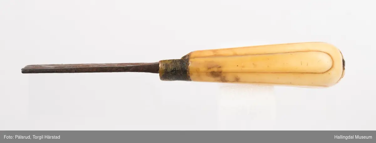 Kniv med etui. 
Etuiet er laget av mørkebrunt lær og ullstoff i grønt, rødt, gult og blått. Den er en tilnærmet rektangulær form som er avrundet i bunn og lokk. Er sydd sammen av to stykker med en ytterside og en innerside. Yttersiden er av mørkebrunt lær med påsydd lærkant. Den bredeste delen kan brettes over som lokk og har en utskjært hjerte- og en utskjært tulipanform. Lokket har på innsiden en lærreim som feste. Begge formene er kantet med lyse sting og foret med rødt ullstoff. 
På innsiden er etuiet foret med grønt ullstoff der de lyse stingene fra formene på lokket er synlig. kniven oppbevares i en av fire lommer som er kantet med grønt, gult, rødt og blått ullstoff. Selve yttersiden av etuiet/eller knivsliren er av mørkebrunt lær, kantet med samme lærkant som yttersiden og lokk, og er dekorert med linjer på sidene. Den er også dekorert med en påsydd lærlomme som er foret med rødt ullstoff som synes på kantene. Sydd med lyse sting og er preget med med et kryss og en V. 

Kniven har et skaft med et utskåret dyrehode (hvalross) og et laget av en hvalrosstann. Noe skadd. Knivbladet er festet gjennom hele lengden av skaftet, er rustent og har avbrekte deler på knivbladet. Knivblad stemplet med P. C./eller O. Westlander.