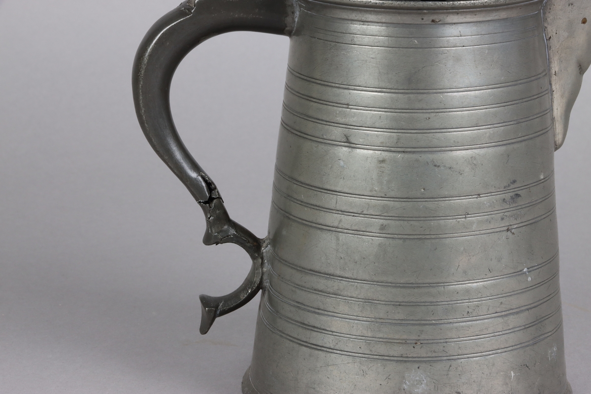 Jug and cover, all in pewter, with conical body  and a loop handle. On the cover knob in the form of a pine cone. On the body sections of horizontal borders. Five hallmarks inside the jug.
