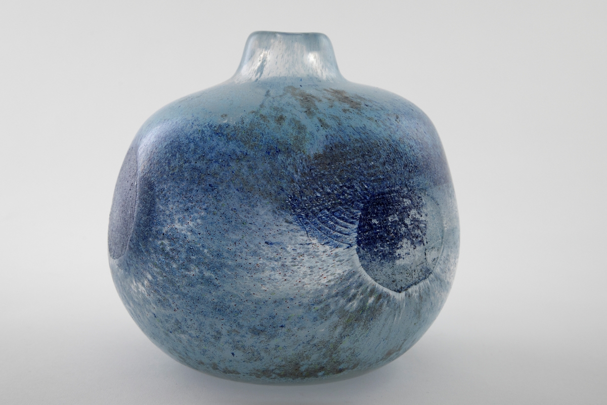 Kuleformet vase med kort hals og liten munning. Klart glass med innlagte metalltråder samt -netting, hvor overflaten er dekorert med blå-, brun- og grønnspettede partier.