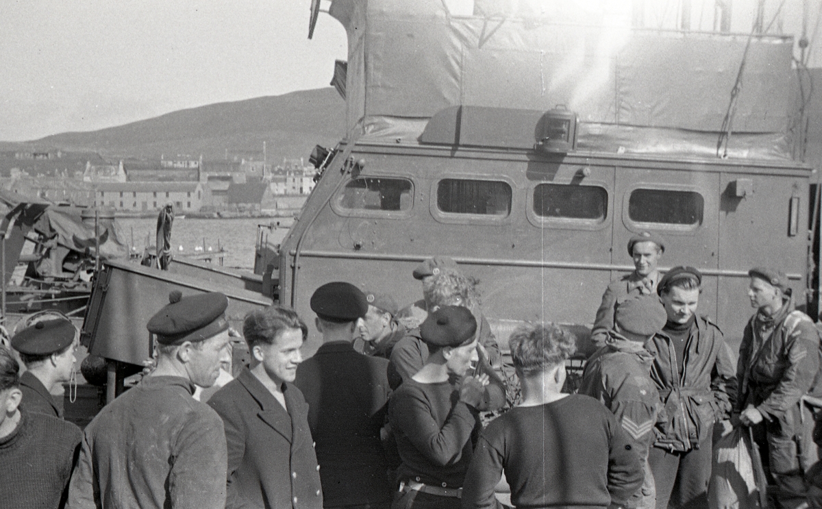 Mannskap fra KNM HITRA  samt Lingekarer på kaien i Scalloway Shetland 14 Mai 1945. KNM Hitra nærmest kaien i bakgrunnen, og sannsynligvis LT Joachim Rønneberg fra Kompani Linge nærmest HITRA med beret og ansiktet mot fotografen. 