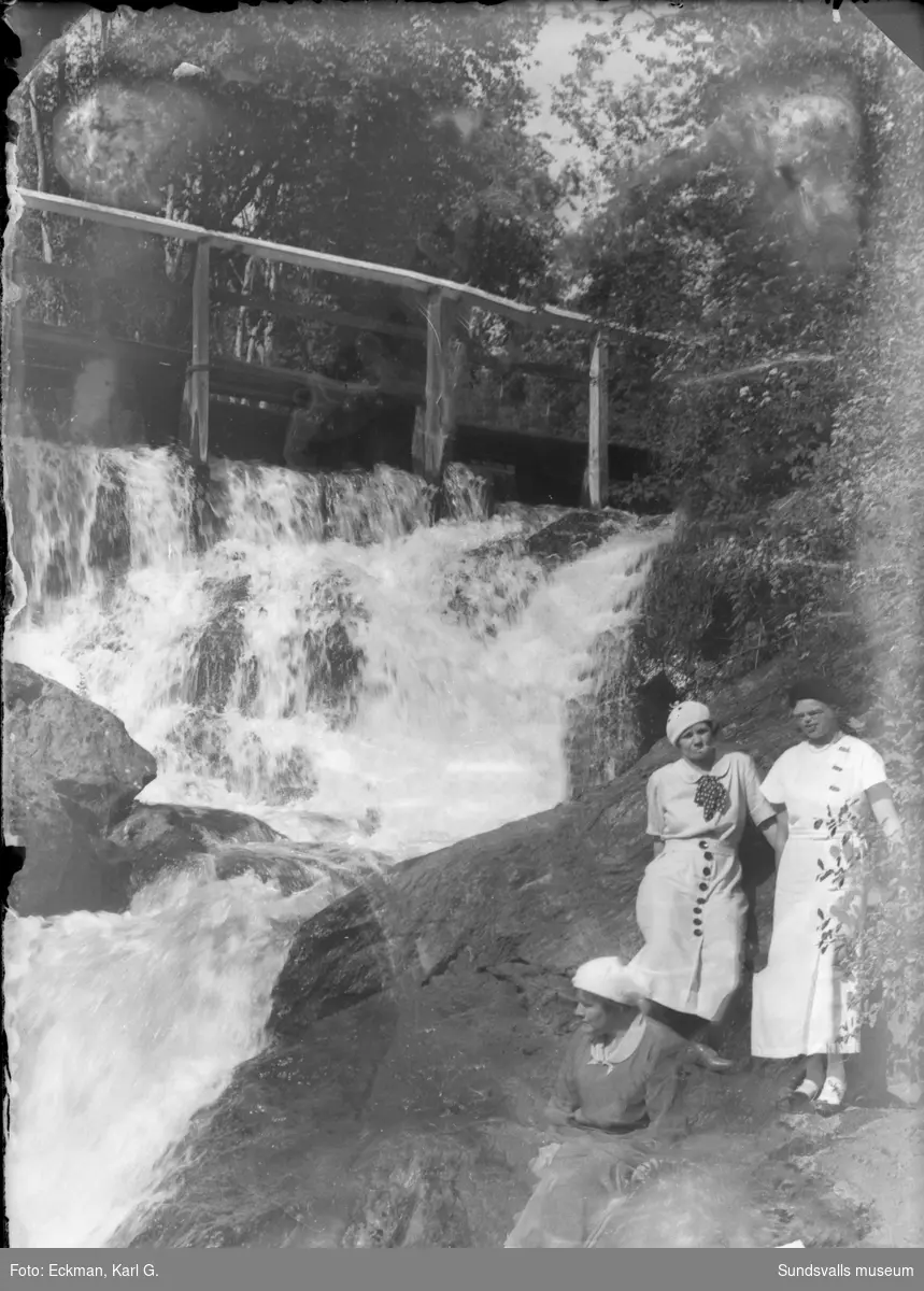 Tre kvinnor intill vattenfallet vid sågdammen i Kvarndalen, Indal. Glasnegativet är väldigt skadat. Ur Karl Eckmans samling.
