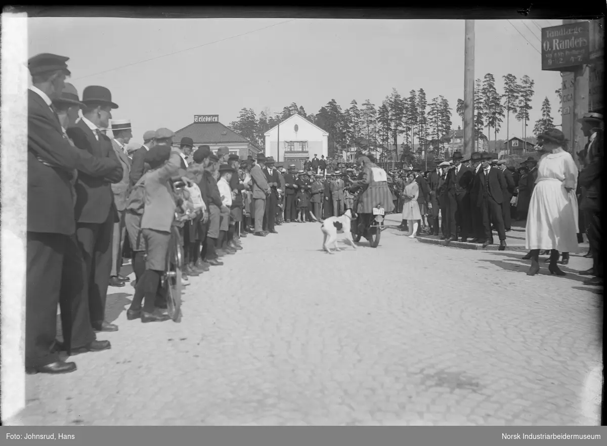 Motorsykkelløp i Notodden i regi av "Notodden & omegns motorsykkelkubb". Publikum langs løpsbane. Mann på motorsykkel distrahert av hund midt i bildet.