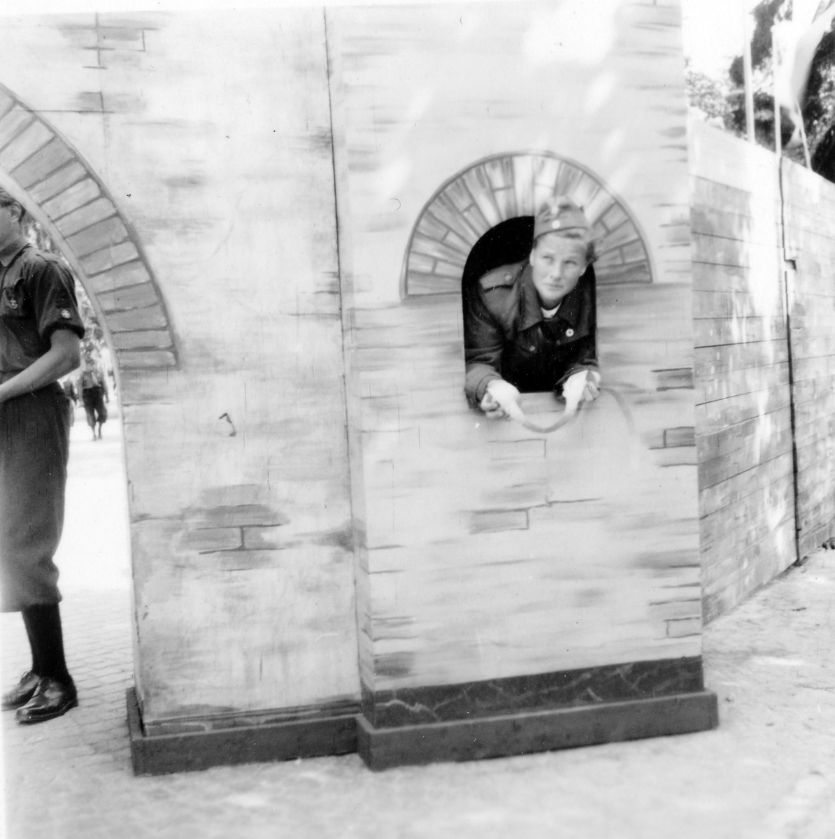 Barnens dag firande i Alingsås 1938. En tonårspojke i uniform och mössa står i ett fönster intill en port i muren och en tonårspojke i samma slags uniform står vid porten.
