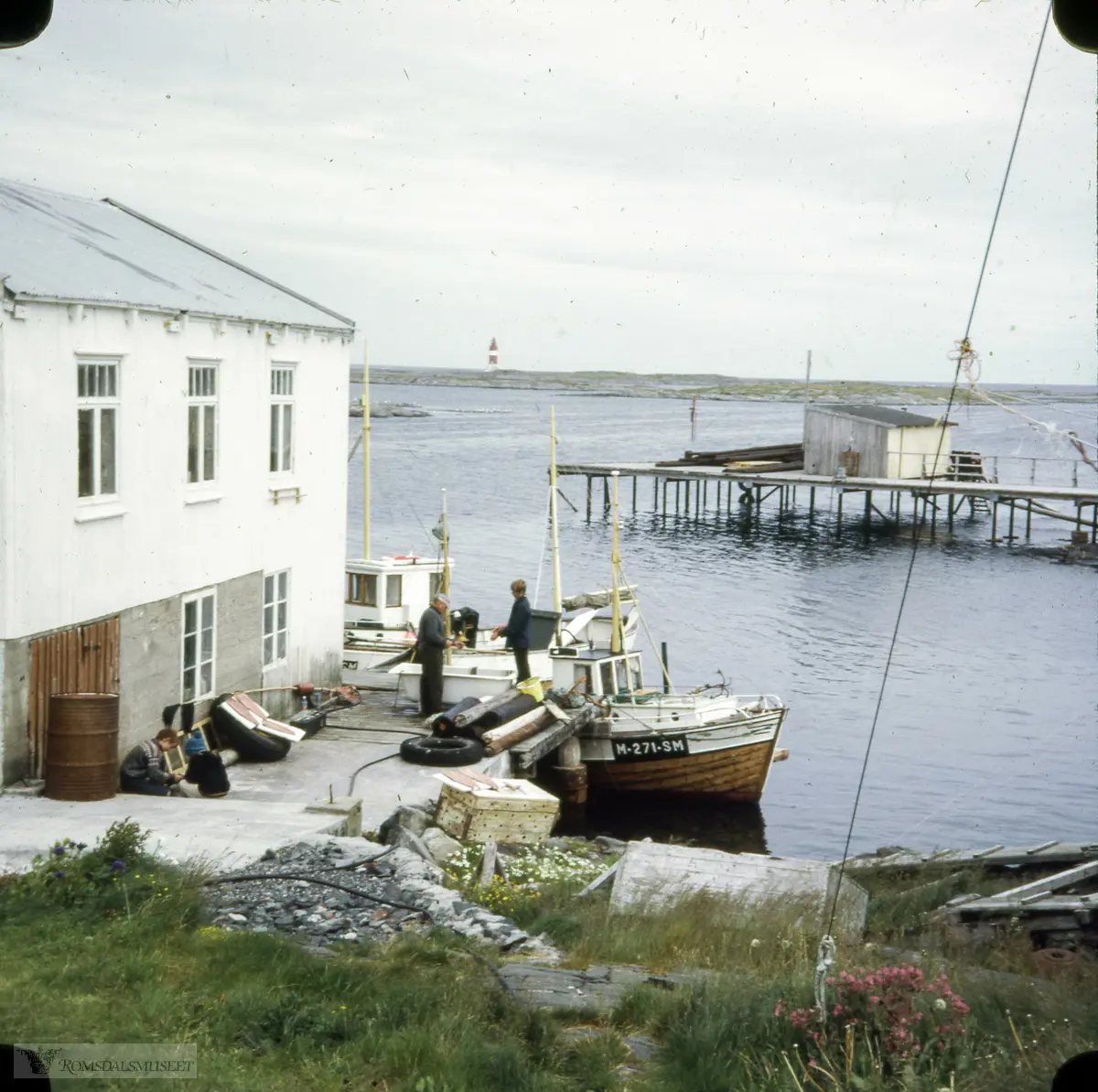 "Veidholmen".Bakkan, Veiholmen, Smøla. Bryggå hans Lars Hagen, (tidligere brygga til «Vågar» i Strand-rederiet.) I bakgrunnen ser vi den gamle Dampskipskaia med lagerskur. Hauggjegla fyr langt der ute.